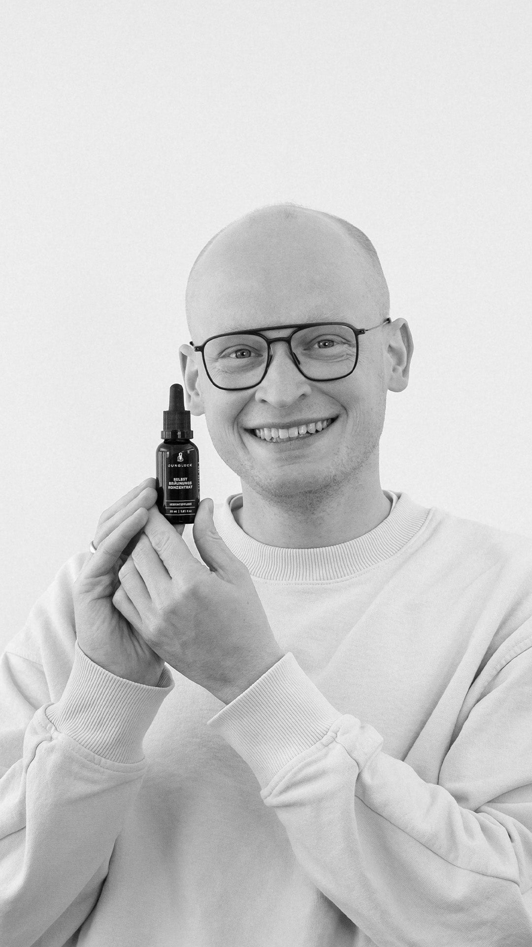 Mann hält eine Braunglasflasche mit dem Produkt Benedikt in der Hand, lächelt in die Kamera.