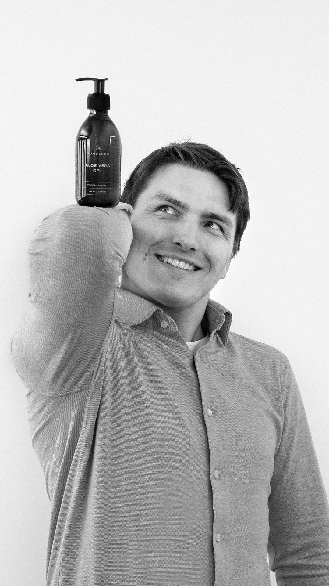 Lächelnder Mann hält eine braune Glasflasche mit Marinus-Hautpflegeprodukt über der Schulter. Schlichte Präsentation.