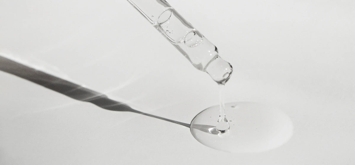 Eine Pipette tropft klares Öl auf eine weiße Oberfläche, mit sanften Schatten.