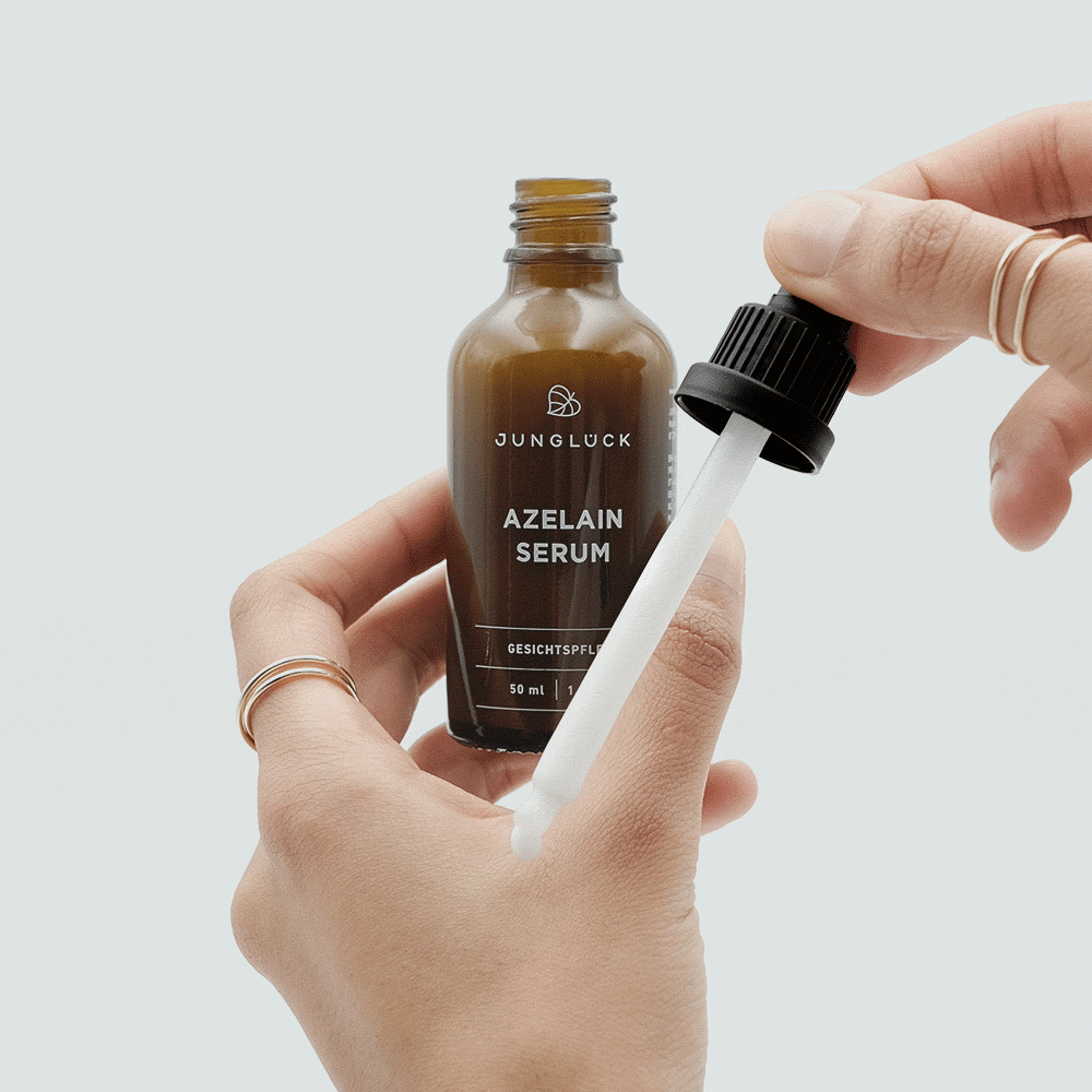 Eine Hand hält das Azelain Serum in einer braunen Glasflasche mit Pipette. Das Produkt hat eine klare Textur.