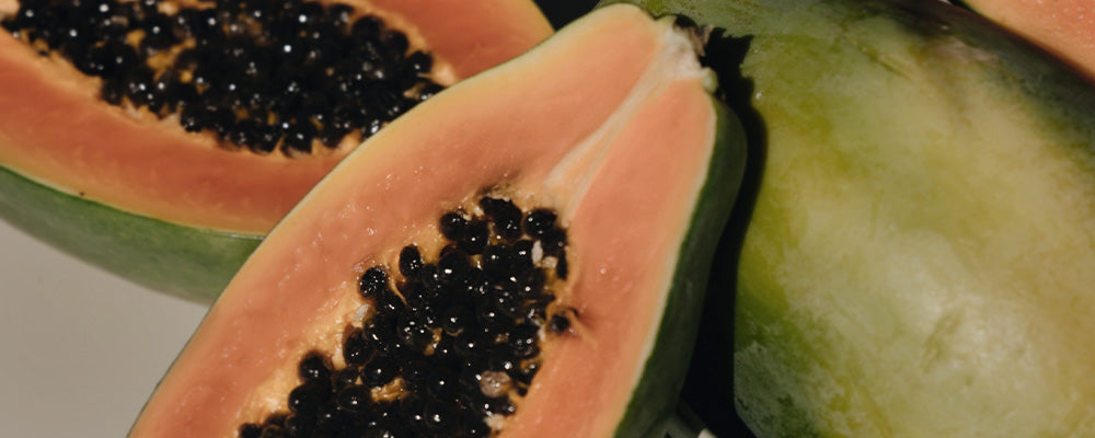 Halbierte Papaya mit orangefarbenem Fruchtfleisch und schwarzen Kernen, umgeben von weiteren Papayas.