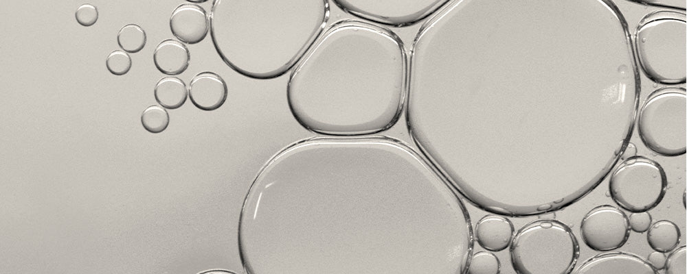 Transparente Tropfen und Bläschen in unterschiedlichen Größen auf einem hellen Hintergrund, die Squalan symbolisieren.