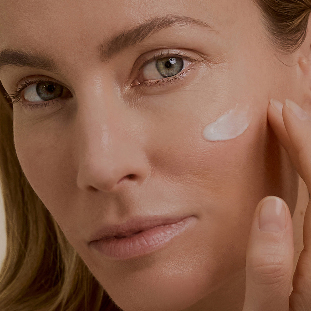 Eine Frau trägt sanft eine Retinal Creme auf ihre Wange auf. Ihr Gesicht zeigt eine ruhige Ausstrahlung.