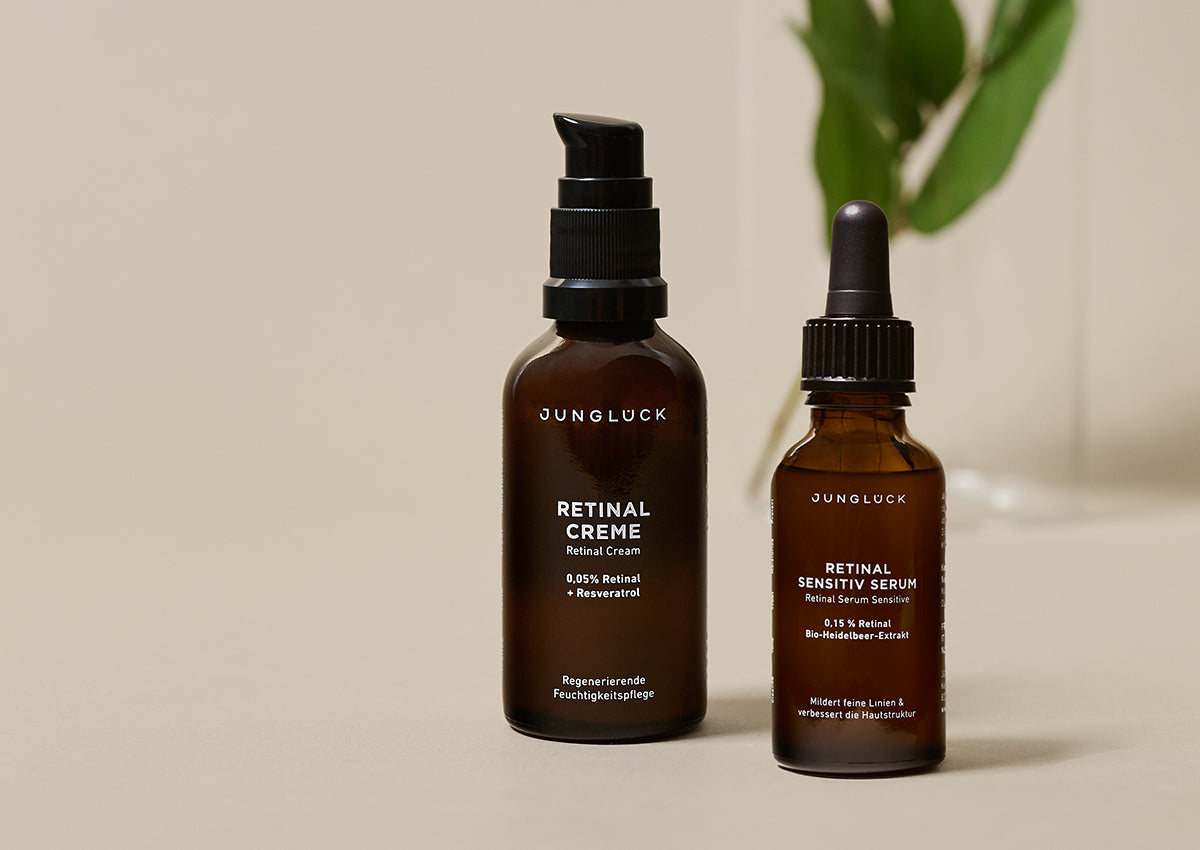 Zwei Produkte von JUNGLÜCK: eine Braunglasflasche mit Retinal Creme und eine mit Retinal Sensitivity Serum. Schlichte,