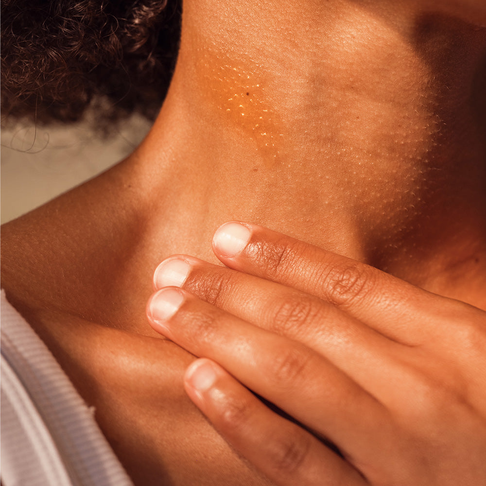 Nahaufnahme einer Hand, die sanft über die Haut am Hals gleitet, die Lichtreflexion zeigt eine gesunde Ausstrahlung.