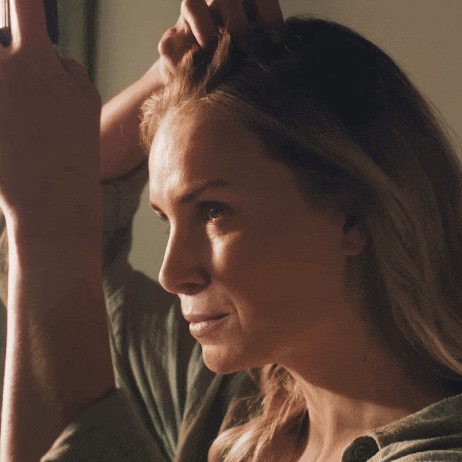 Eine Frau setzt Trockenshampoo im Haar an, die Haarpartien werden sorgfältig angehoben. Natürliches Licht betont ihr Gesicht.