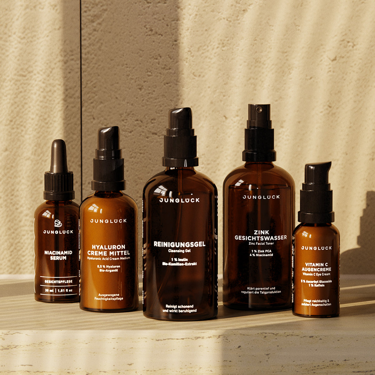 Fünf Braunglasflaschen von JUNGLÜCK, darunter Hyaluron Creme Mittel, Zink Gesichtswasser und Vitamin C, auf einer