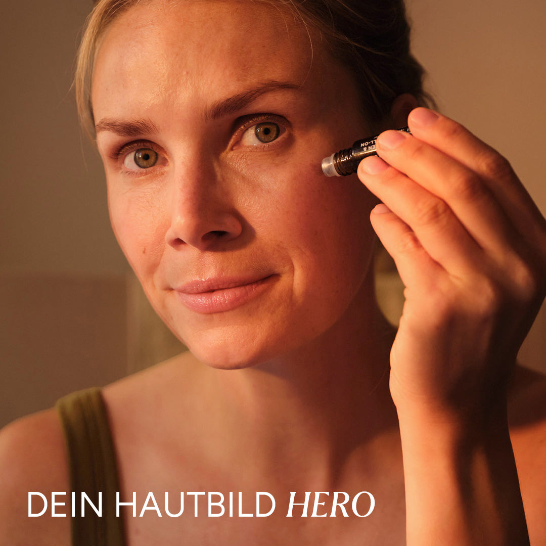 Eine Frau trägt einen Roll-On auf ihre Haut auf. Sie blickt in den Spiegel und lächelt sanft.