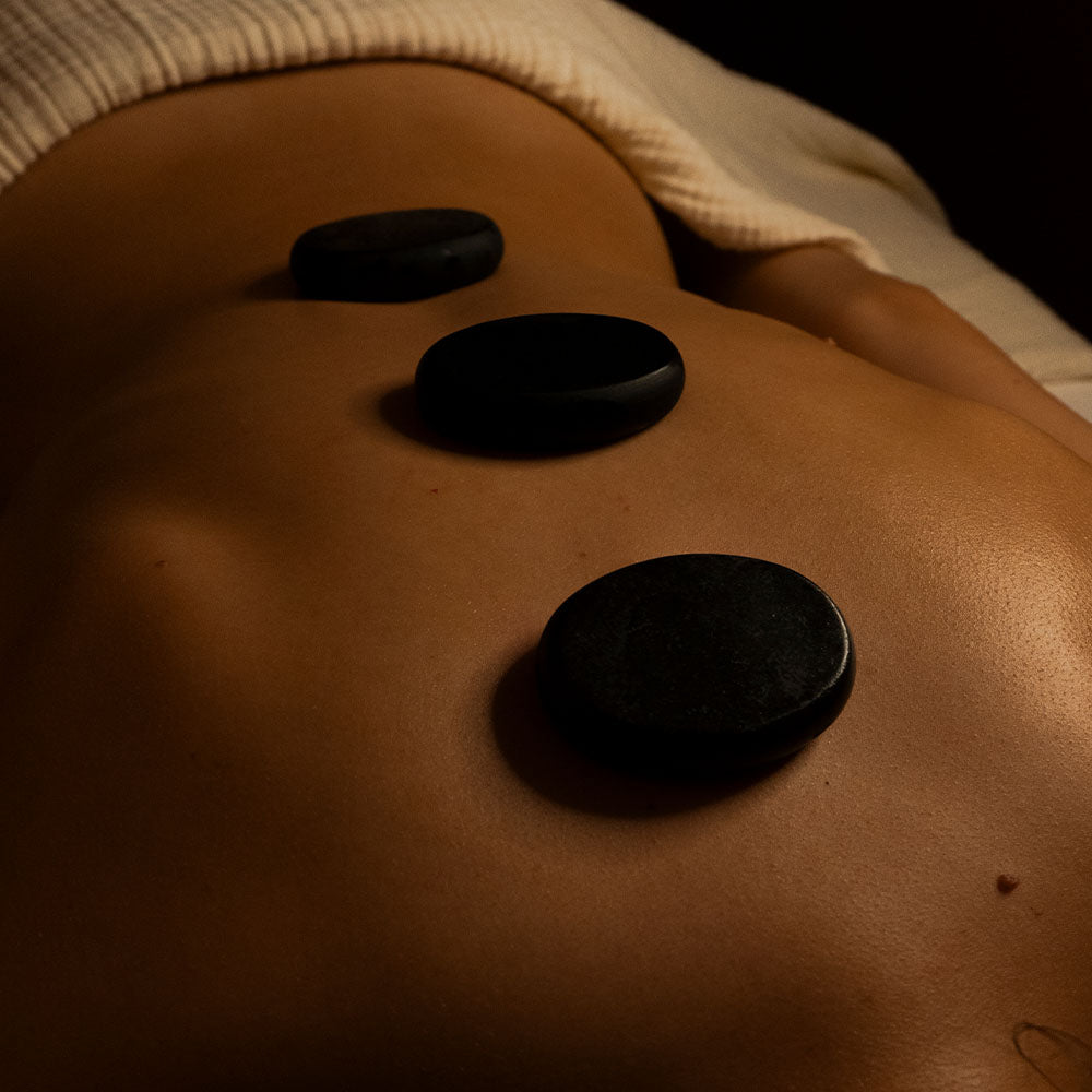 Drei glatte, schwarze Steine liegen auf dem Rücken einer Person während einer Hot Stone Massage.