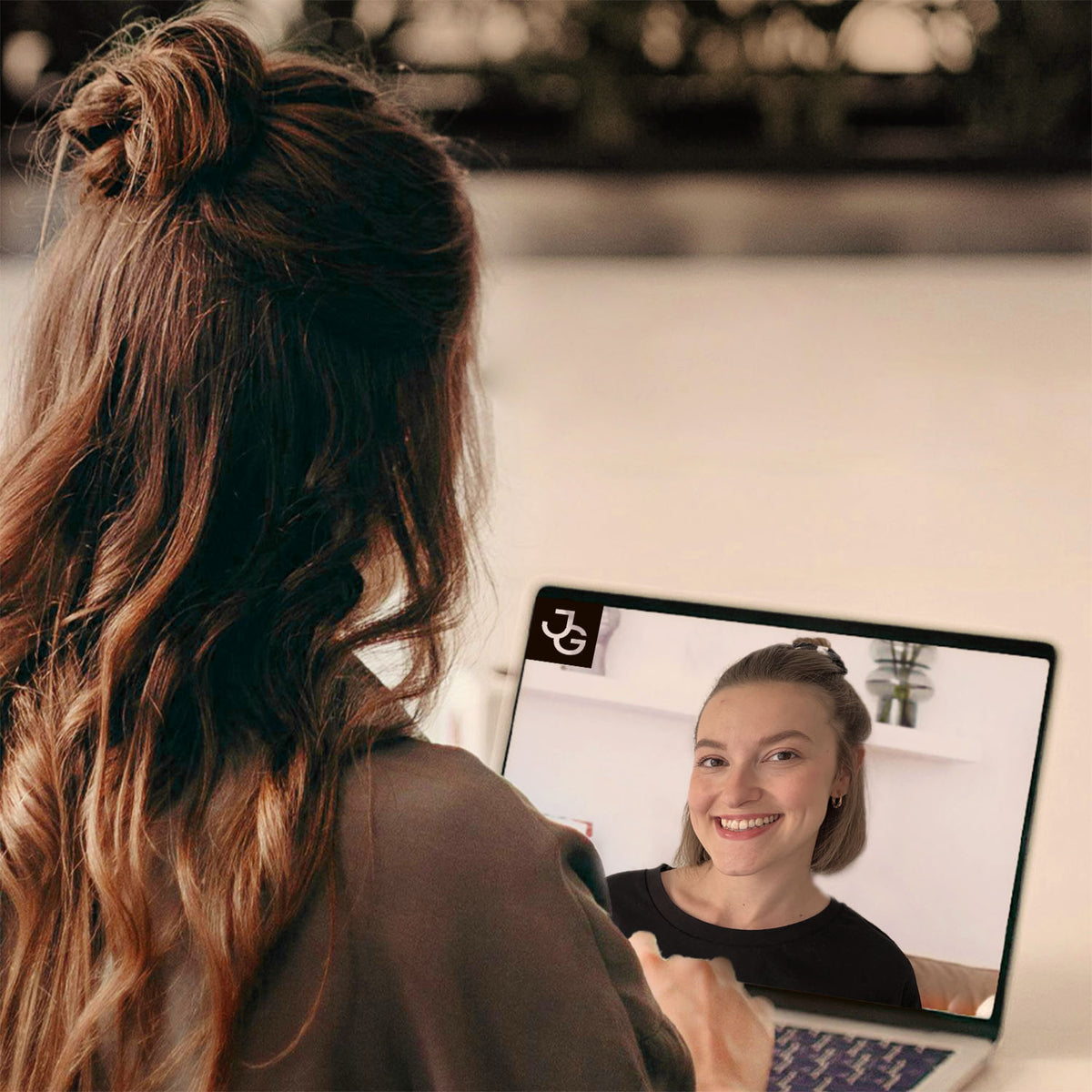 Frau mit langen Haaren sieht auf einen Laptop-Bildschirm mit einer Videoberatung. Ruhige Atmosphäre.