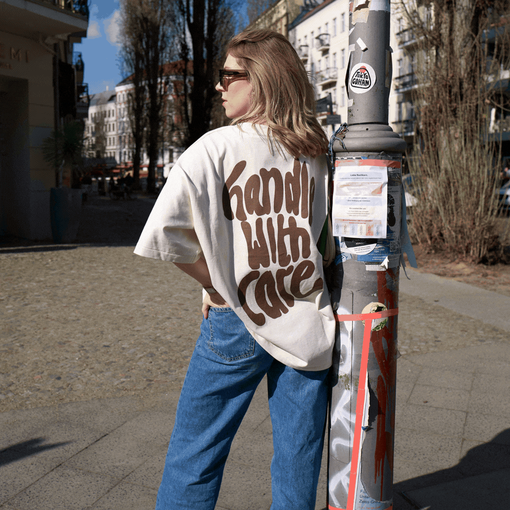 Frau im lässigen Streetstyle-Outfit mit T-Shirt in Cremefarbe und Jeans, steht vor einem Poller in einer urbanen Umgebung.