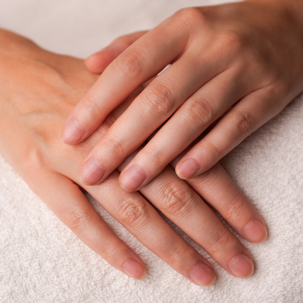 Nahaufnahme von Händen ohne Nagellack, sanft auf einem Handtuch abgelegt, gepflegt und glatt.