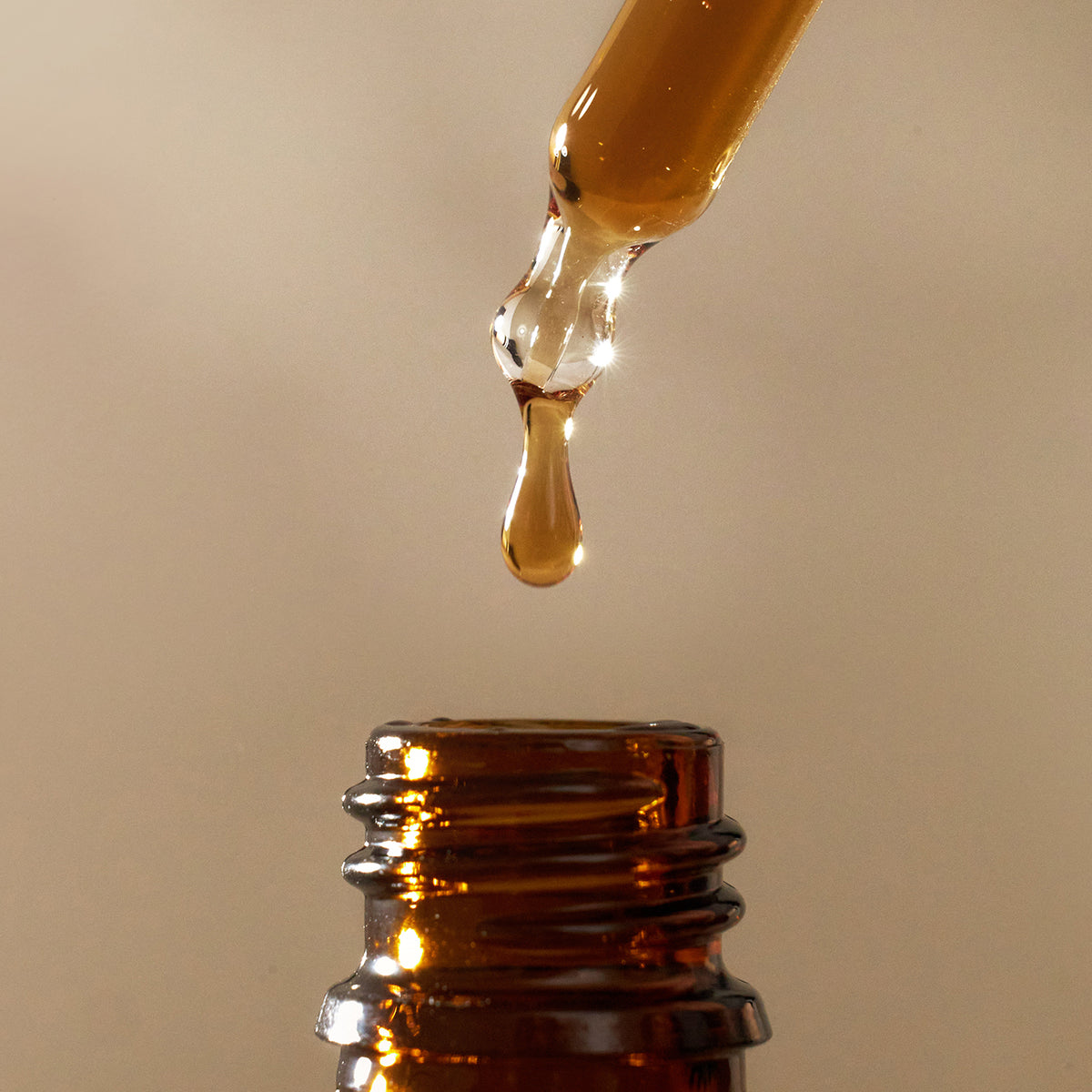 Braunglasflasche mit Pipette, die einen Tropfen flüssiger Hautpflege abgibt.