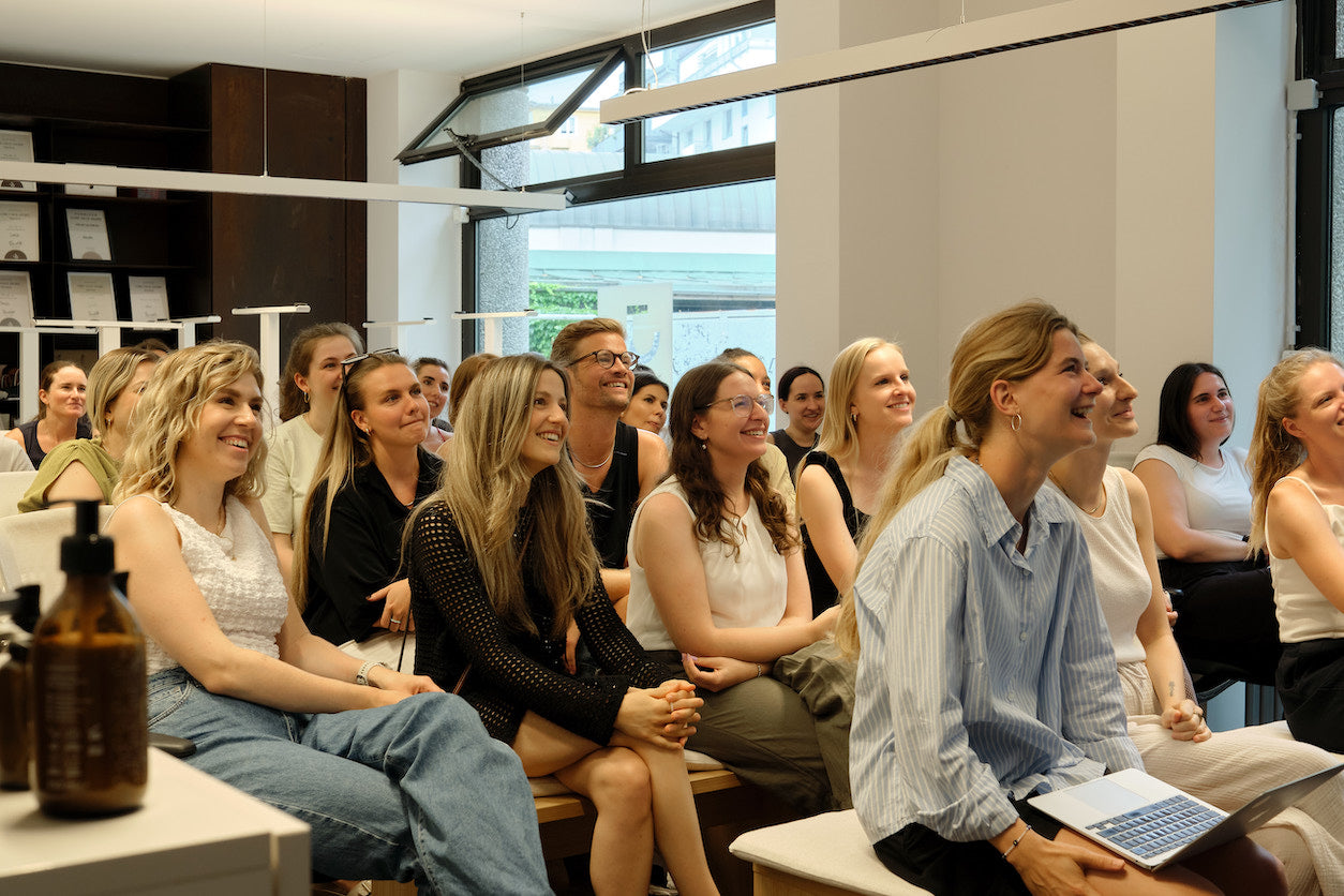 Gruppe von Frauen in einem hellen Raum, die sitzen und aufmerksam an einem Vortrag teilnehmen. Einige lächeln und wirken