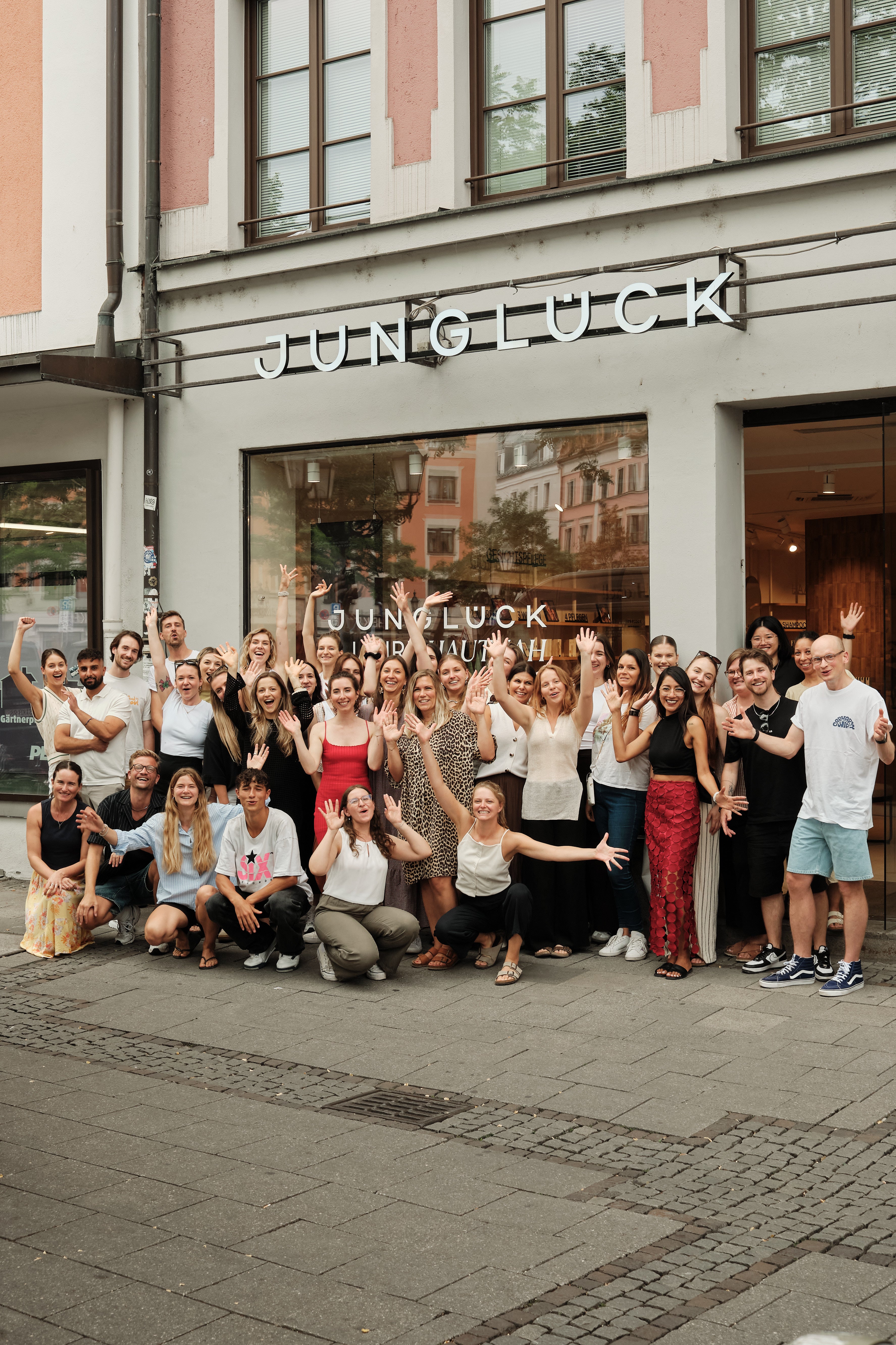 Gruppenfoto des JUNGLÜCK-Teams vor dem Geschäft, alle lächeln und winken.