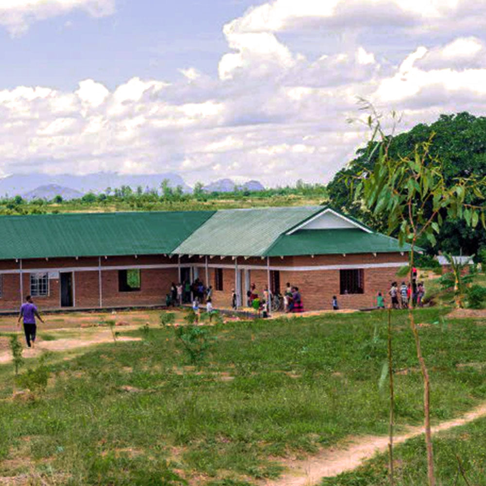 Ein neues, helles Gebäude in Malawi, umgeben von Grünflächen und Menschen, die sich vor und um das Gebäude versammeln.