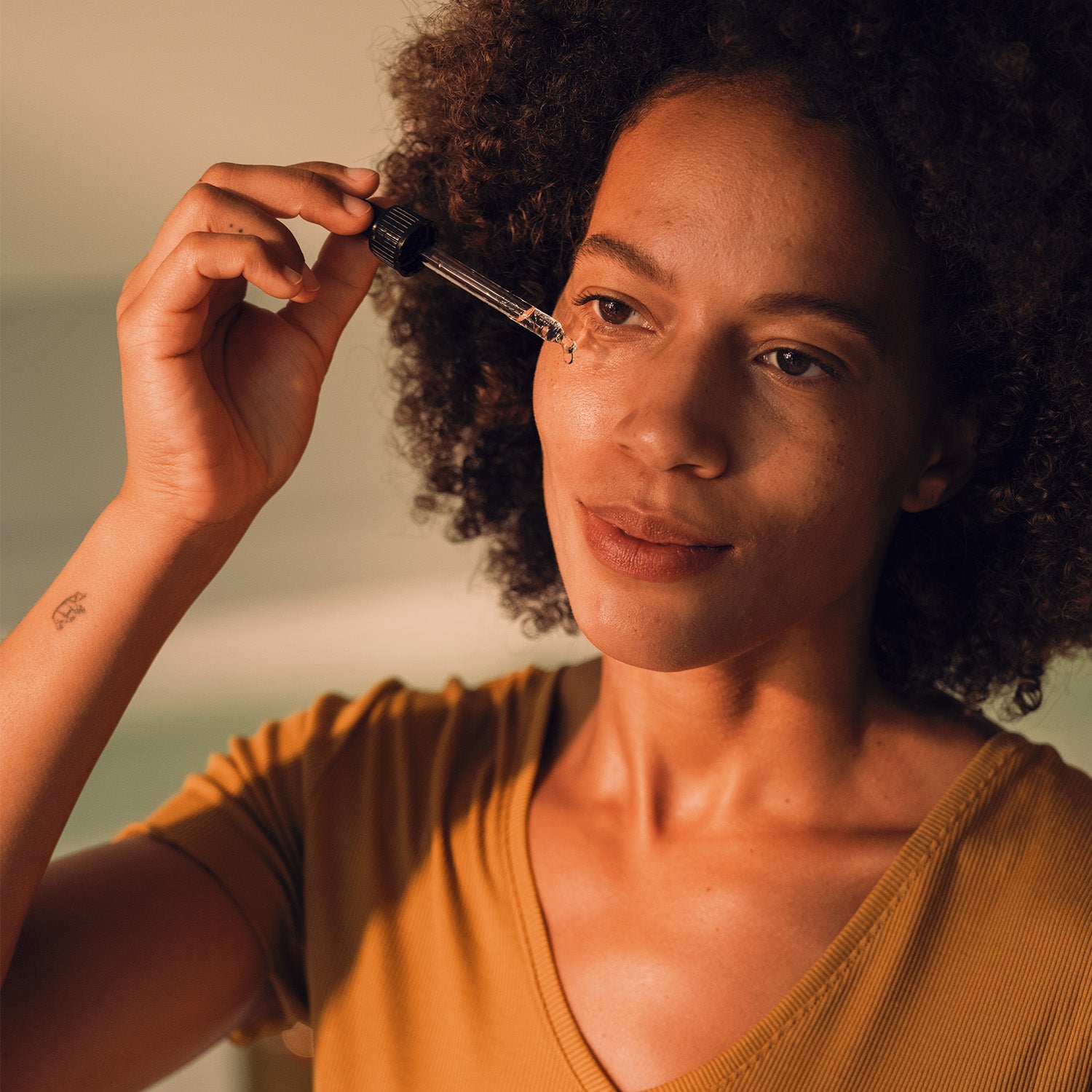 Eine Frau mit lockigem Haar trägt das Seren Model auf ihr Gesicht auf. Sie hält eine Pipette in der Hand.