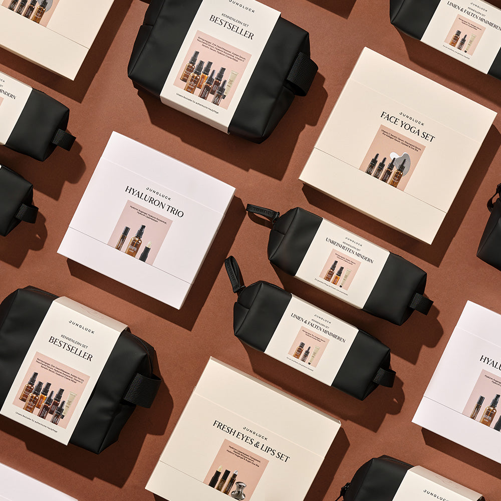 Das Bild zeigt das Hyaluron Trio Geschenkset sowie weitere JUNGLÜCK Produkte in eleganten Verpackungen auf braunem