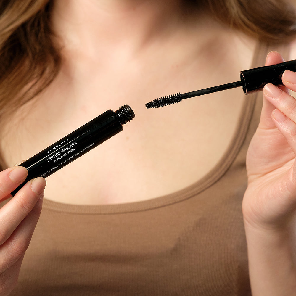 Model hält JUNGLÜCK Peptide Mascara geöffnet in die Kamera