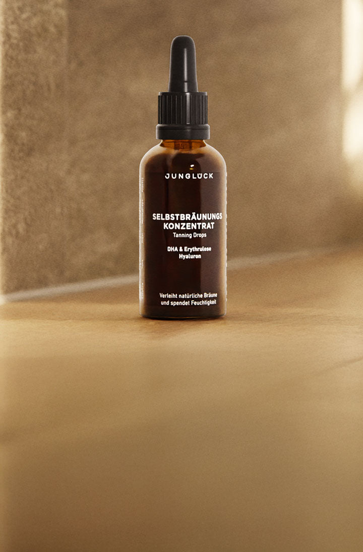 Braunglasflasche mit Tanning Drops, zeigt den Produktnamen „Selbstbräunungs Konzentrat“ und Inhaltsstoffe.
