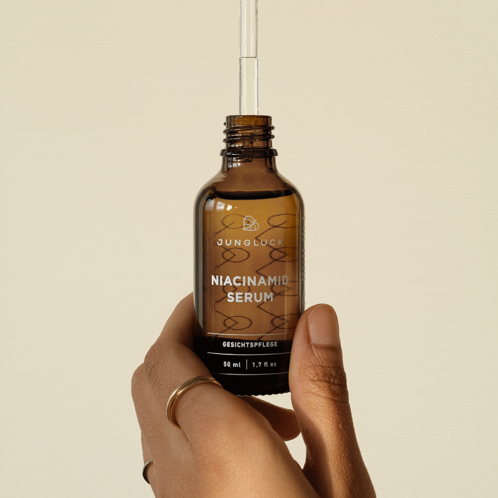 Braunglasflasche mit Pipette, gefüllt mit einem Niacinamid-Serum, in einer Hand gehalten. Hintergrund in neutralem Farbton.