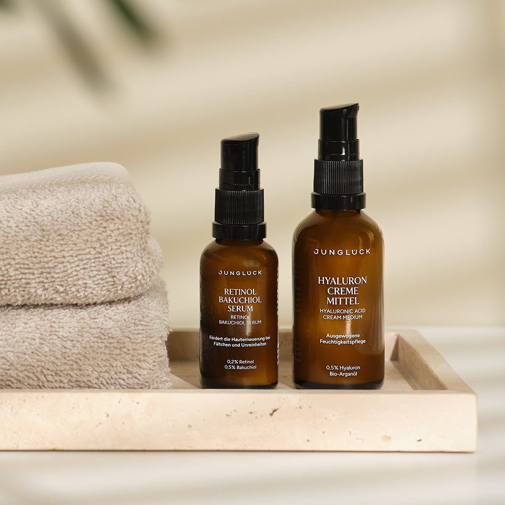 Braunglasflaschen mit JUNGLÜCK Retinol Bakuchiol Serum und Hyaluron Creme Mitle, präsentiert auf einem Plateau neben einem