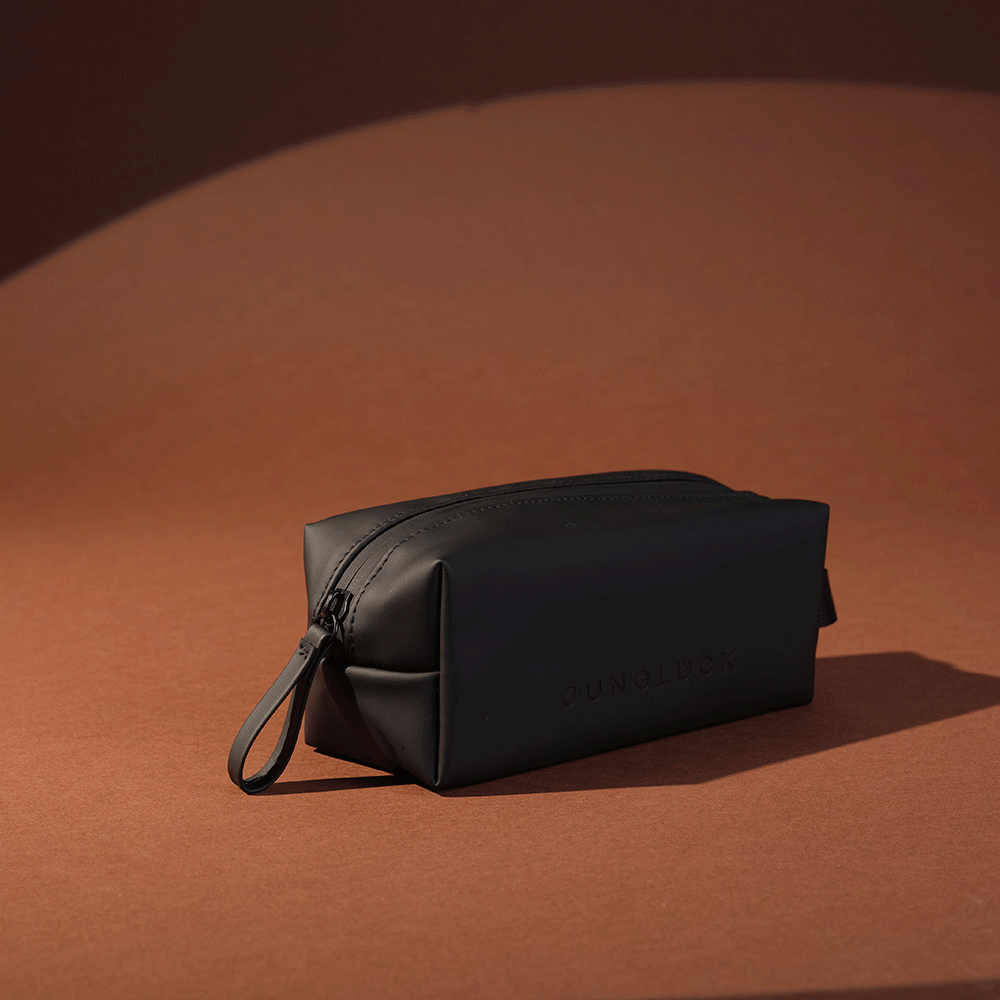 Schlichte schwarze Kosmetiktasche mit Reißverschluss, aus faltbarem Material, auf braunem Hintergrund.