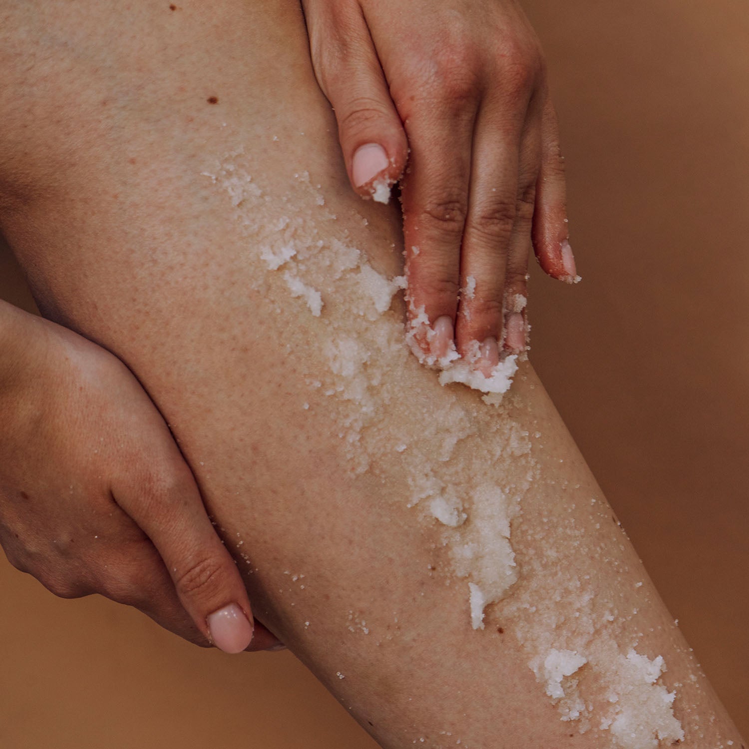 Hände tragen das Magnesium Body Peeling auf das Bein auf, das mit Peelingkristallen bedeckt ist.