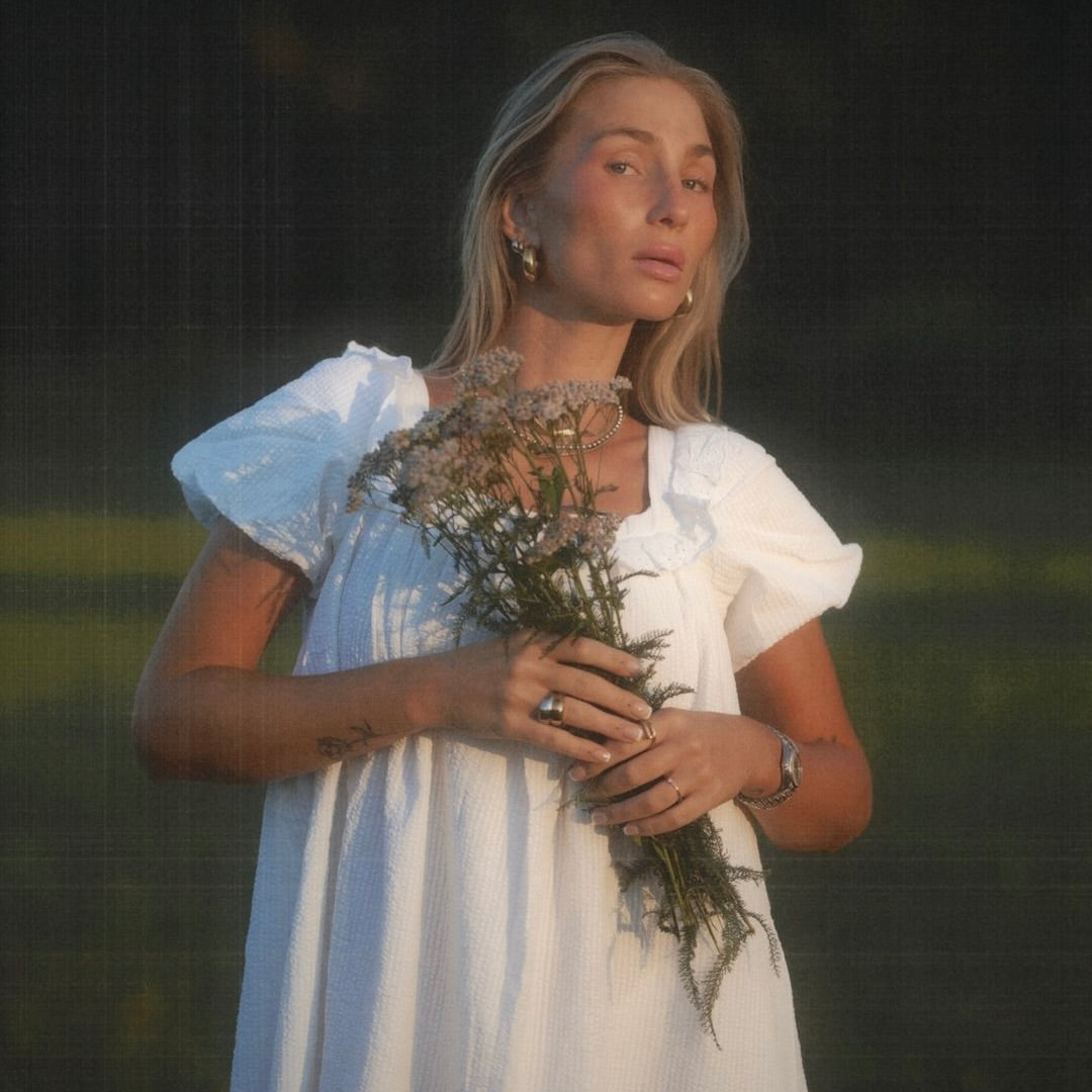 Frau in weißem Kleid mit Puffärmeln hält einen Blumenstrauß. Zarte, natürliche Ausstrahlung.