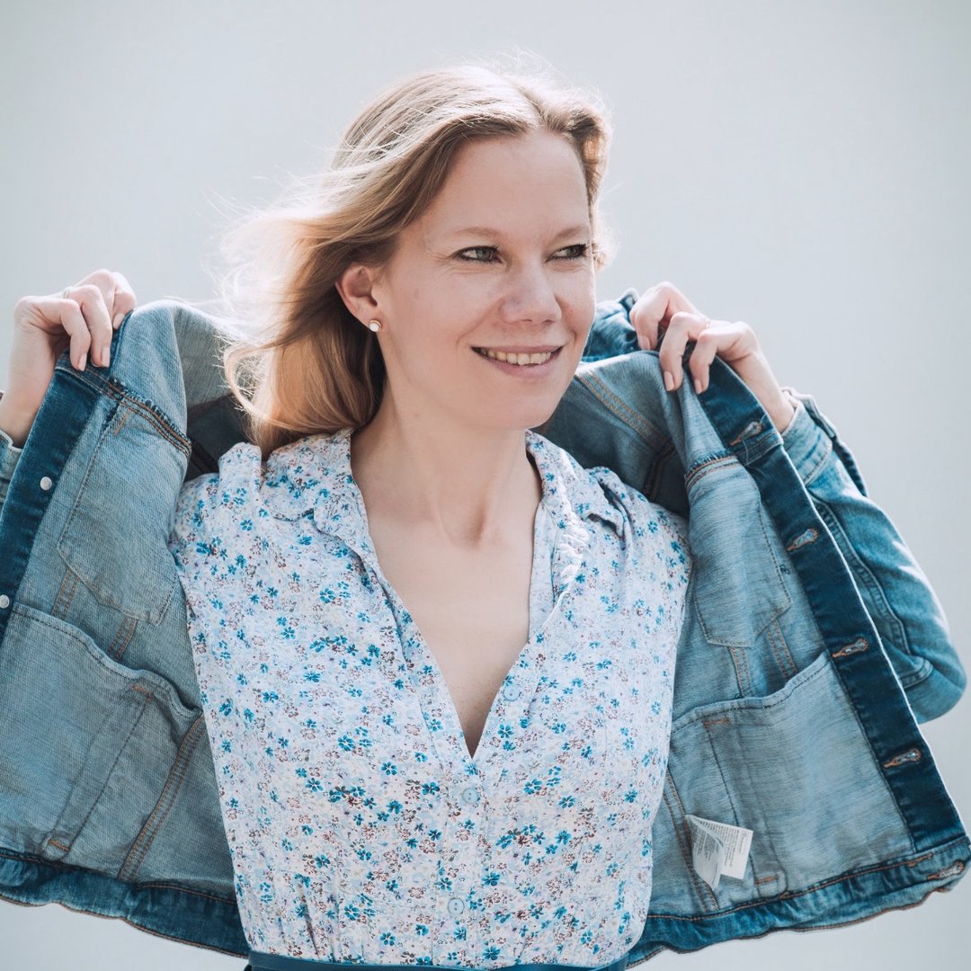 Frau mit blauer Jeansjacke und bluse mit Blumenmuster, lächelt in sanftem Licht.