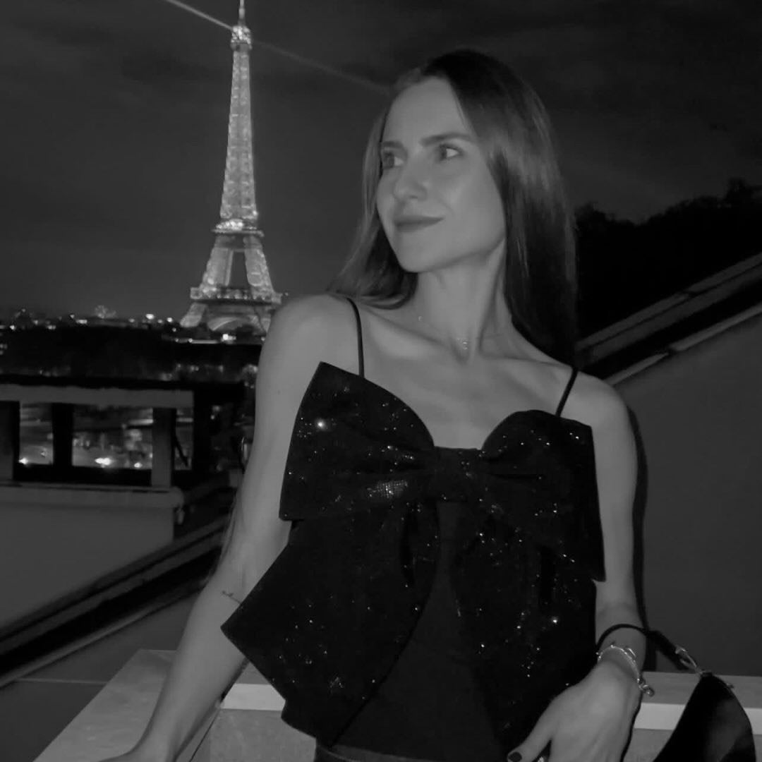 Frau mit glitzerndem Top und Schleife vor der beleuchteten Eiffel-Turm-Silhouette bei Nacht.