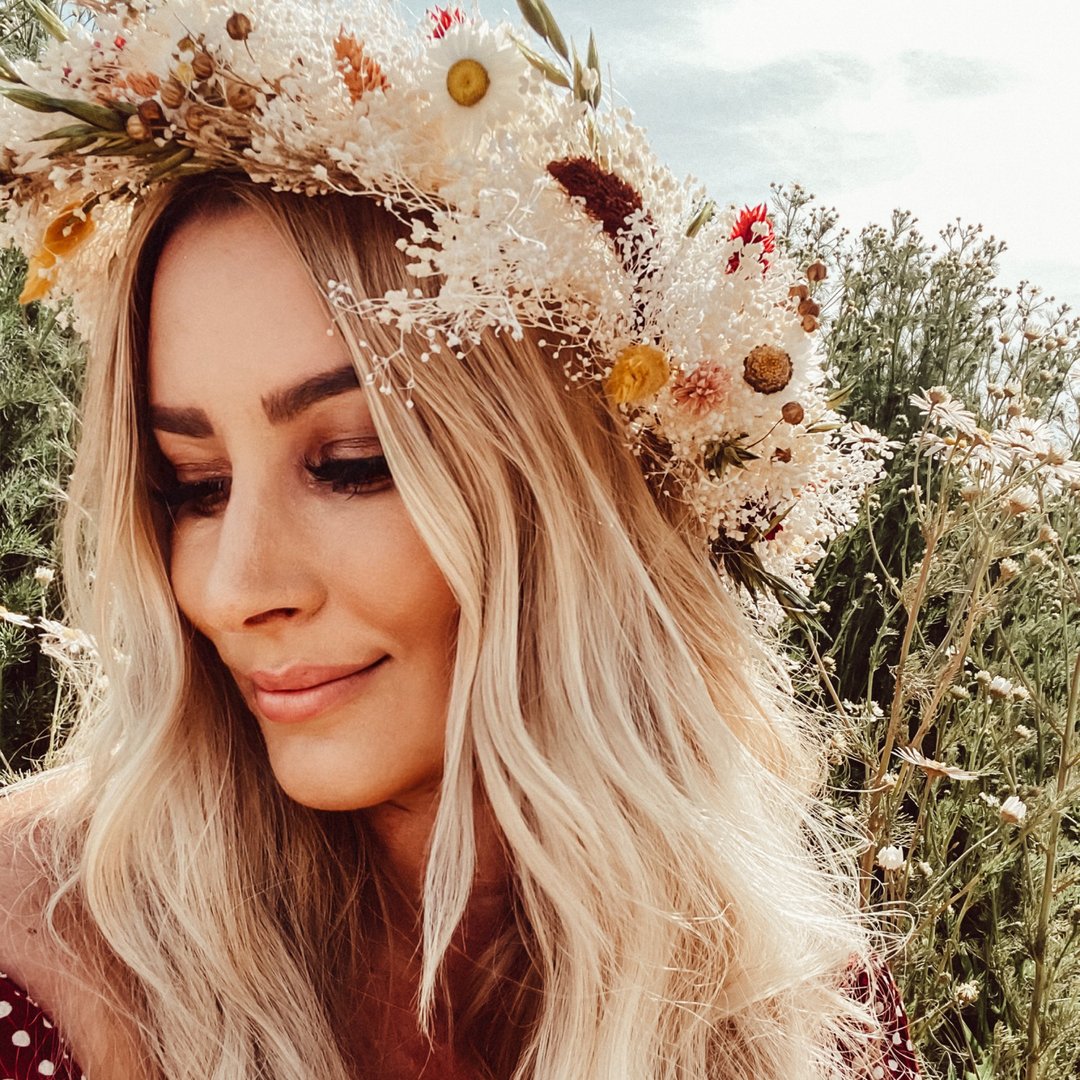 Frau mit blonden Haaren und einem Blumenkranz aus getrockneten Blumen im Freien.