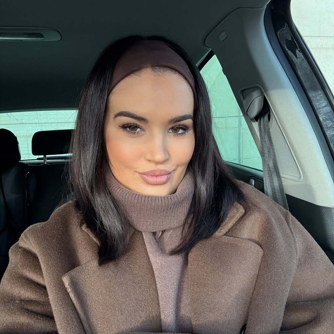 Eine Frau mit langen, dunklen Haaren und einem lässigen, warmen Ensemble aus braunen Tönen sitzt im Auto.
