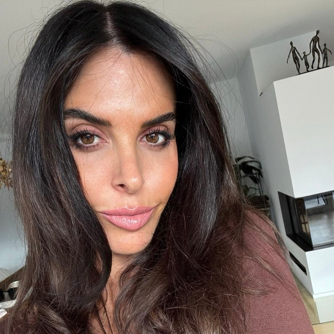 Liebliche Nahaufnahme einer Frau mit langen, dunklen Haaren und einem sanften, natürlichen Make-up. Sie lächelt selig in