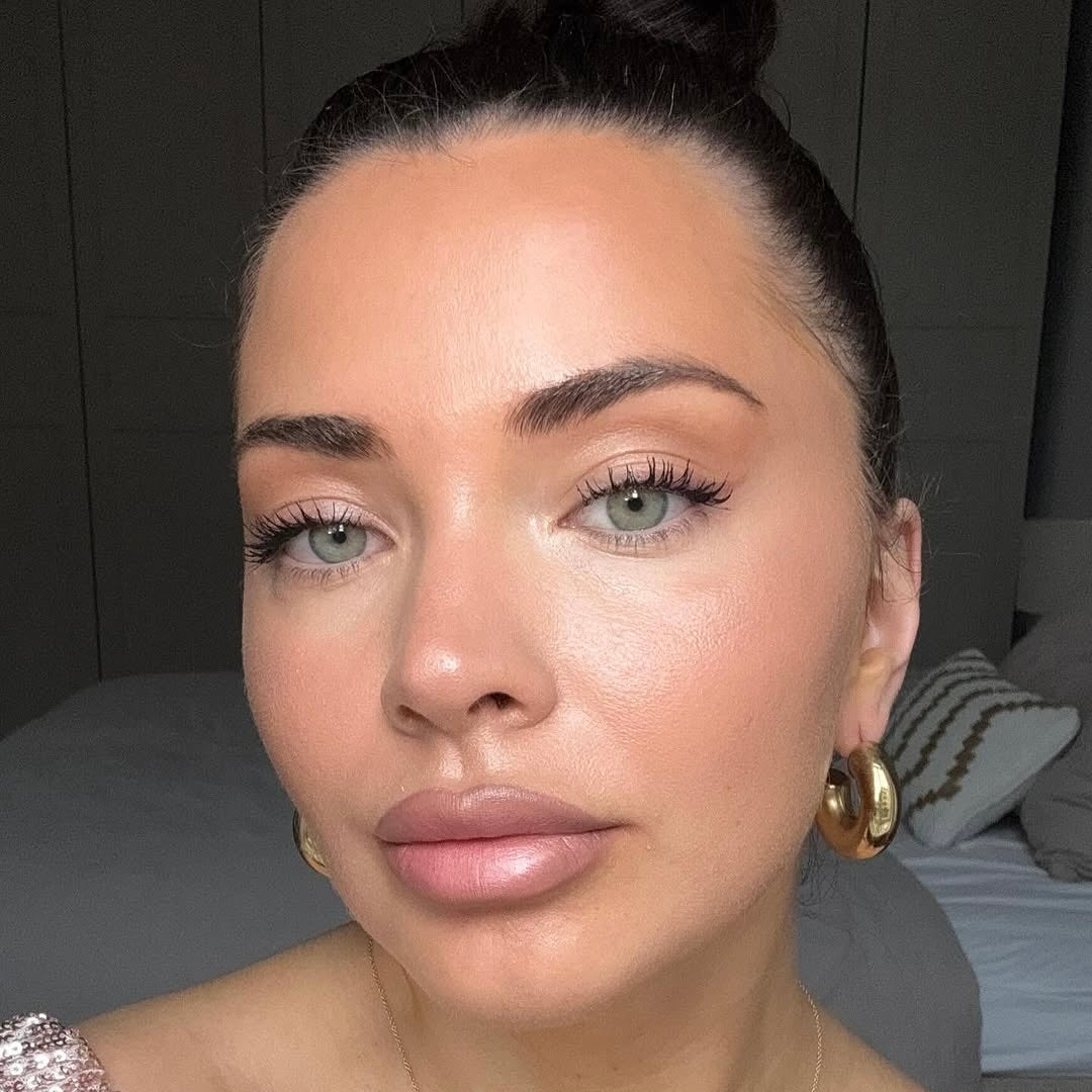 Frau mit natürlichem Make-up und eng anliegendem Dutt, trägt goldene Ohrringe, sanfter Hautton.