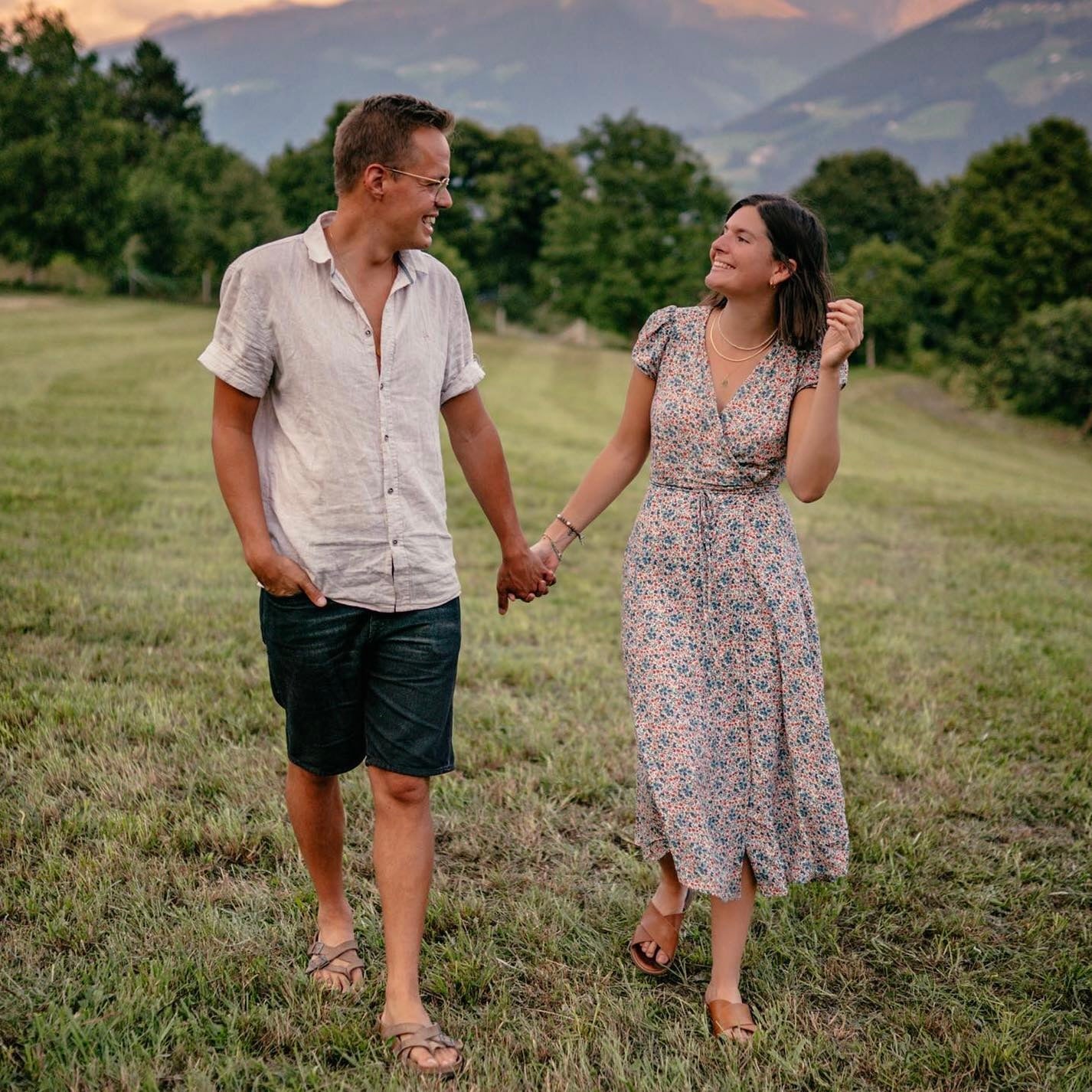 Ein Paar, das Hand in Hand auf einer Wiese spaziert. Die Frau trägt ein florales Maxikleid und die Männer ein lässiges Hemd.