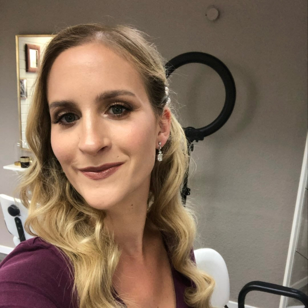 Ein strahlendes Porträt einer Frau mit langen, blonden Locken. Sie trägt einen make-up und hat ein leichtes Lächeln. Im
