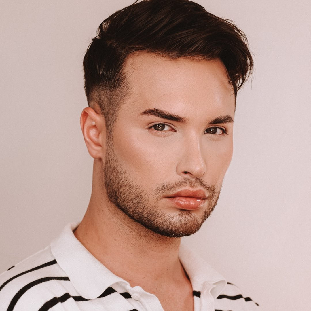 Portrait eines Mannes mit kurzen Haaren, in gestreiftem Poloshirt vor einem hellen Hintergrund.