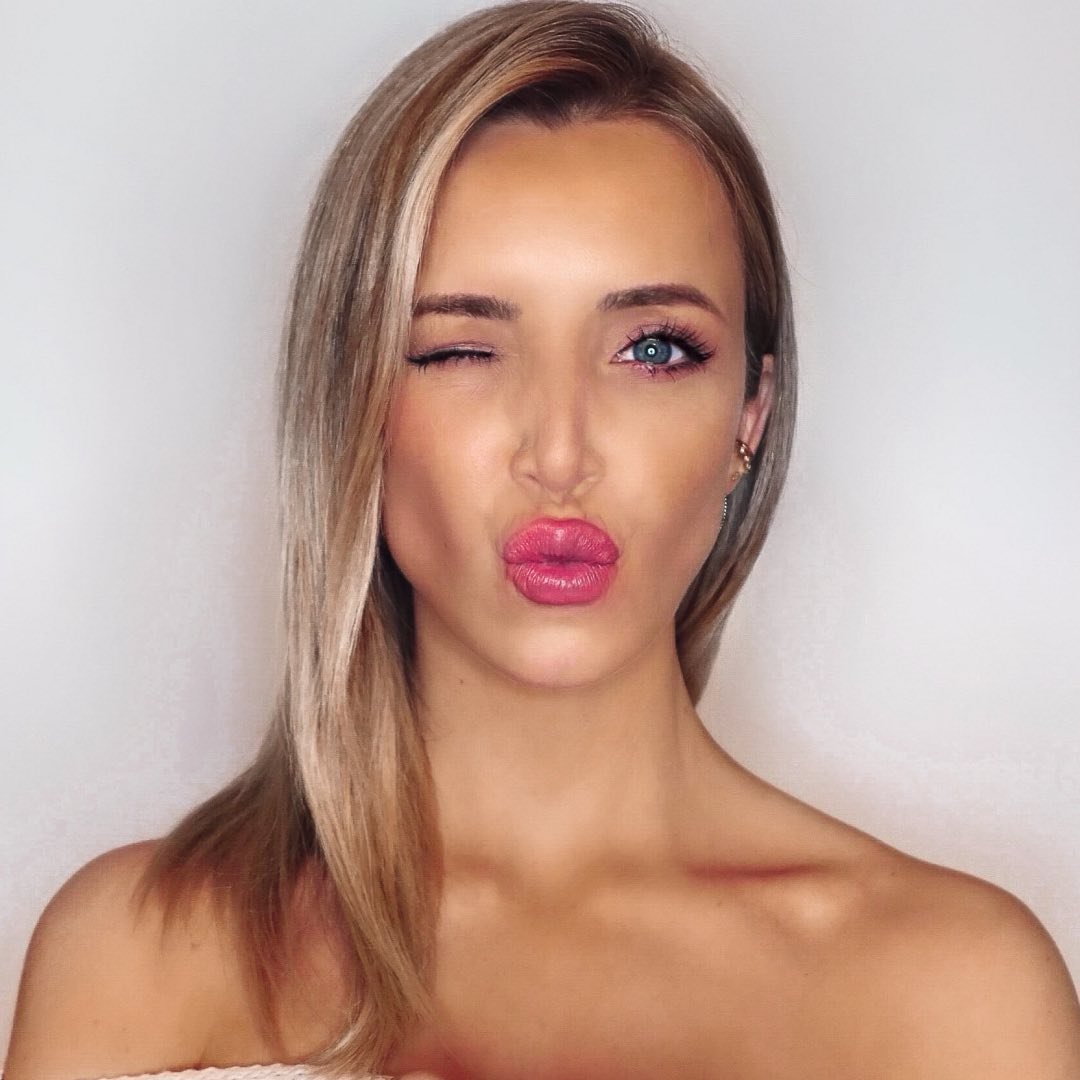Nahaufnahme einer Frau mit blonden Haaren, die mit vollem, glänzendem Lippenstift einen Kussmund formt.