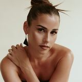 Dame mit dezentem Make-up und schickem Schmuck, die einen ruhigen Blick in die Kamera wirft.