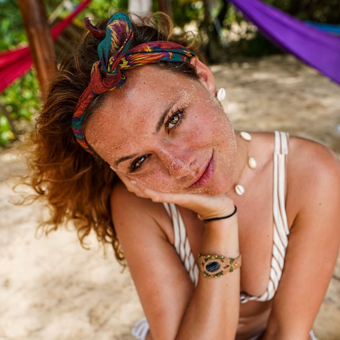 Frau mit lockigem Haar und buntem Stirnband, entspannt im Freien, umgeben von einem natürlichen Ambiente.